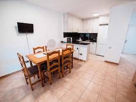 A compact kitchen with a dining area, a flat-screen TV mounted on the wall, and a small island with a microwave.