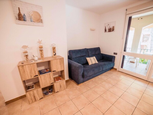 Un salon avec un canapé bleu, des étagères en bois et un sol carrelé.