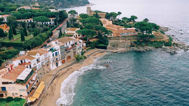 An aerial view of a coastal town with buildings along the beach, a prominent tower, and rocky coastline. - Apartament Reformat a 2 Minuts de la Platja (Palafrugell)