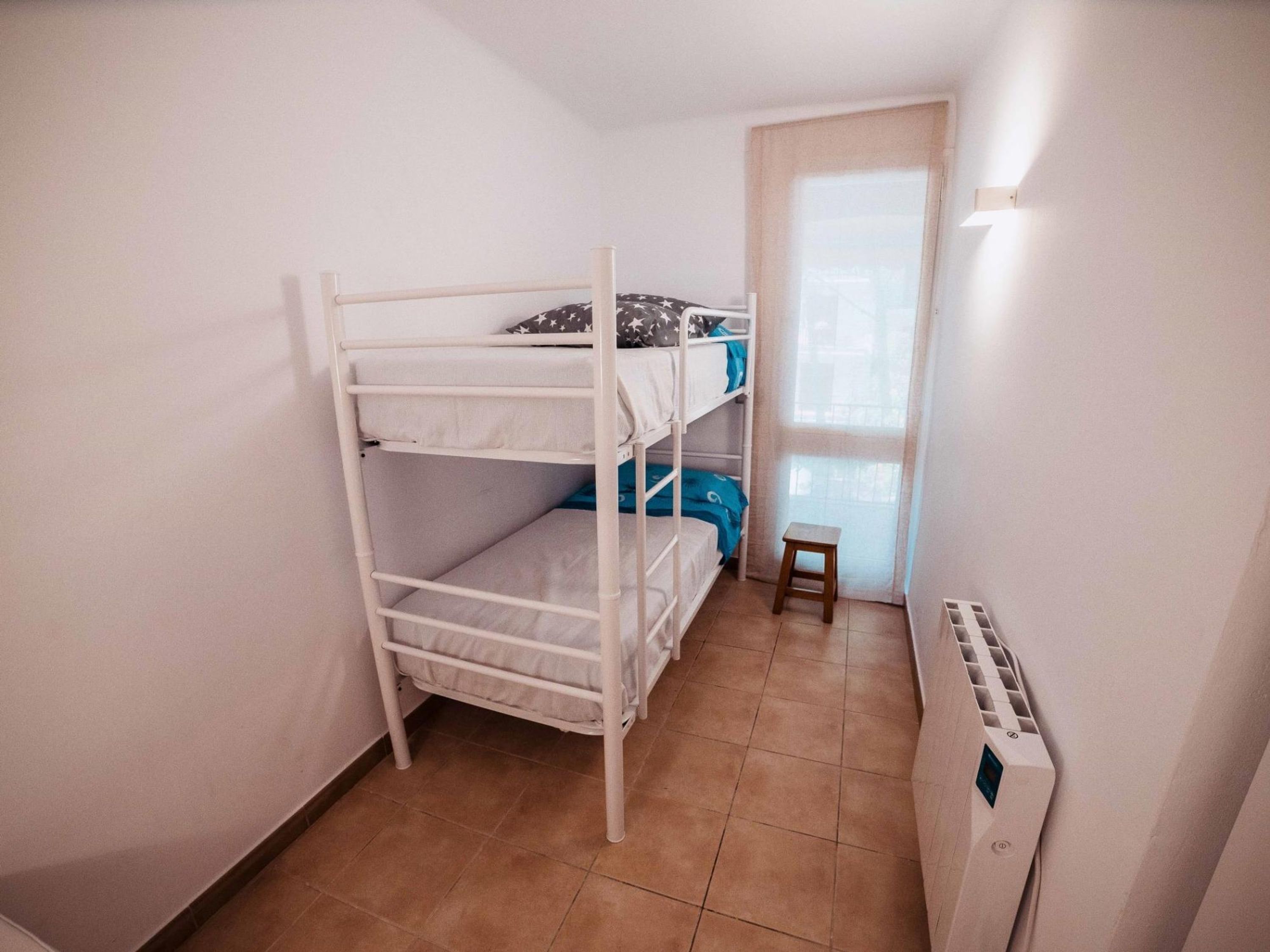 A bunk bed room with a window, a radiator, and a small stool.