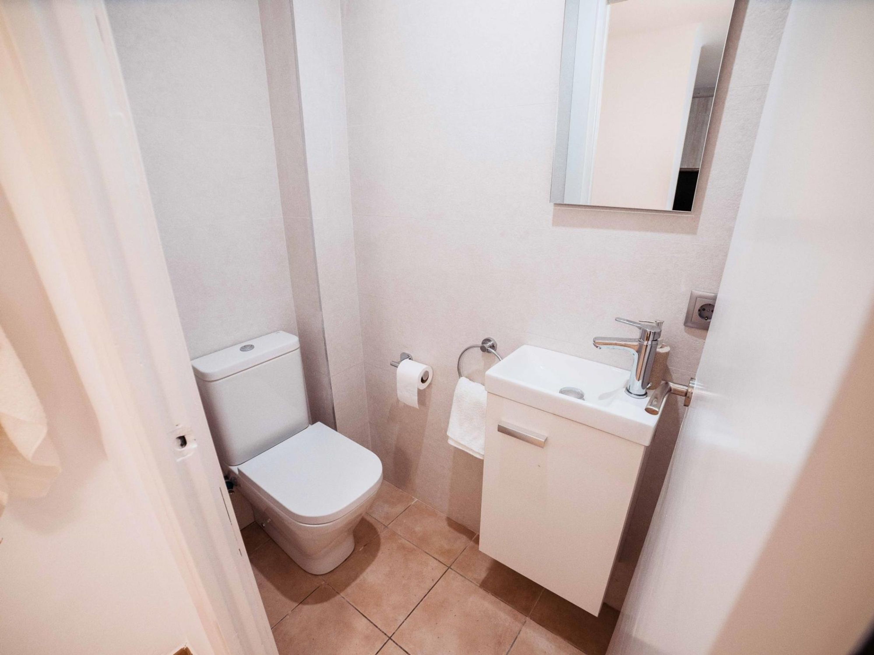 A small, clean bathroom with a toilet, sink, and mirror.