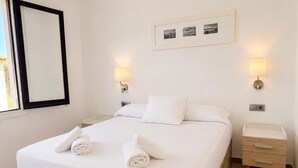 A hotel room with a large bed, two bedside tables, a nightstand, a framed photo on the wall, and a window with a black frame.