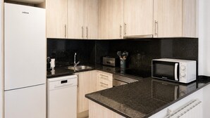 A modern kitchen with light wood cabinets, a black countertop, a dishwasher, a microwave, and a stove.