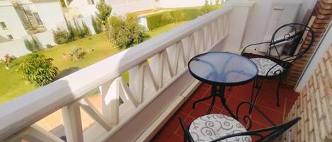A balcony with two chairs and a small table, overlooking a residential area with houses and greenery.