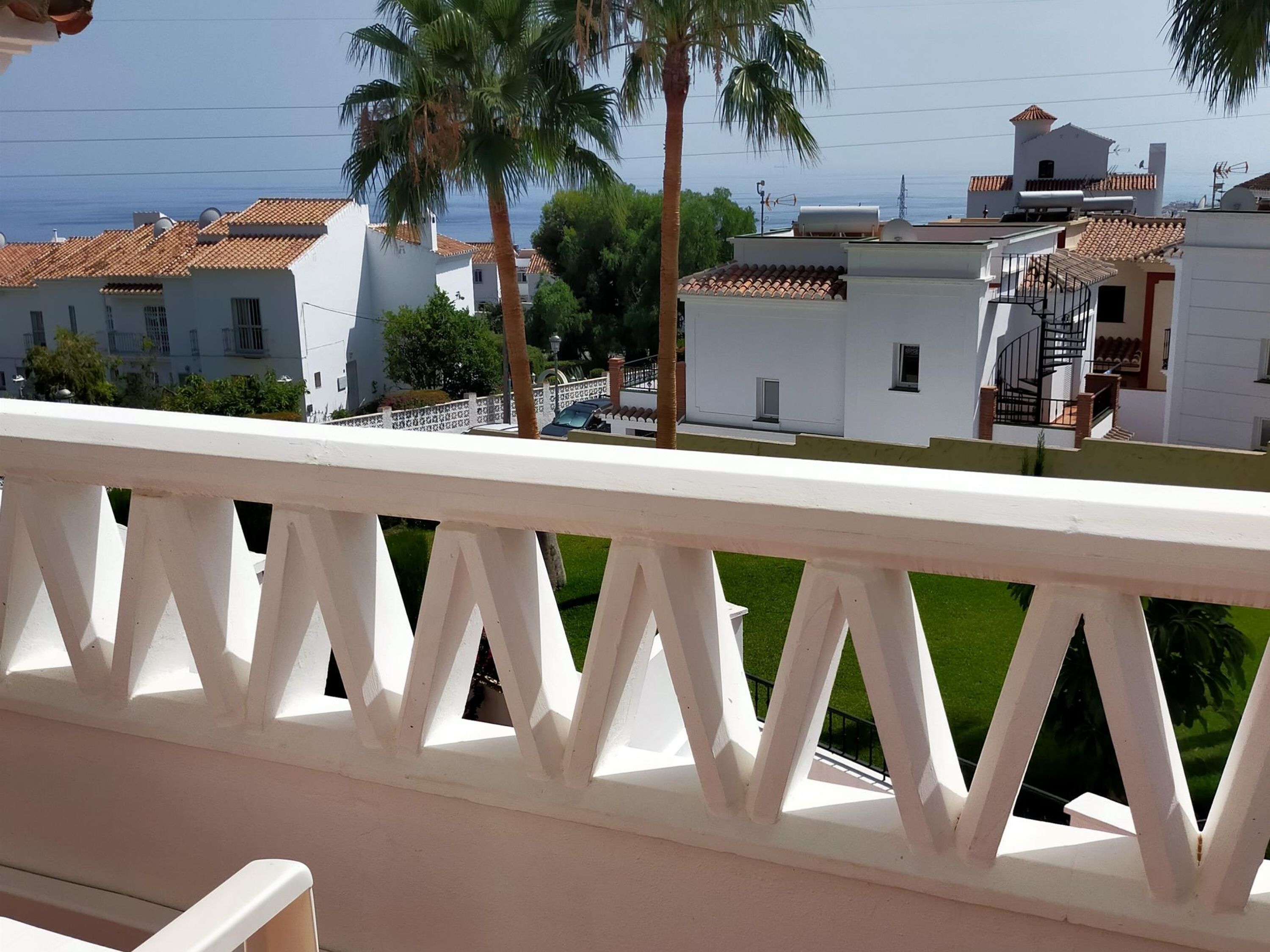 Varanda com guarda branco com vista para área residencial com edifícios brancos e palmeiras.