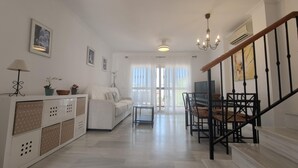 A spacious living room with a white sofa, a dining table, and a staircase. - Casa Cipreses 4 Nerja (Nerja)