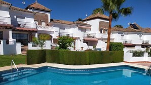 A swimming pool with a tiled edge, surrounded by white buildings with red-tiled roofs and balconies. - Casa Cipreses 4 Nerja (Nerja)