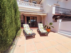 Une terrasse avec deux chaises longues, une plante en pot et un bâtiment blanc doté d’un balcon.