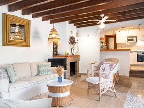 A living room with a sofa, wicker chairs, a fireplace, and a kitchen area with a microwave. - CAN Cusina Charming House With Swimming Pool (Santanyi)