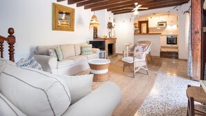 Una sala de estar acogedora con un sofá, sillones y una chimenea. Se ve una cocina con microondas y horno al fondo.