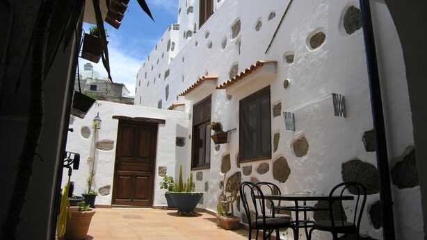 A courtyard with a white building featuring stone accents, a wooden door, and potted plants.