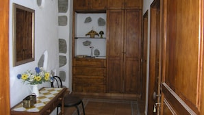 A room with a wooden cabinet, a stone wall, a tiled floor, and a small table with a vase of flowers.