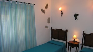 A room with two single beds, a curtain, a wall-mounted lamp, and a small table with a lamp.
