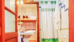 Un baño con puerta de madera, un lavamanos blanco, inodoro y cortina de ducha con estampado verde.