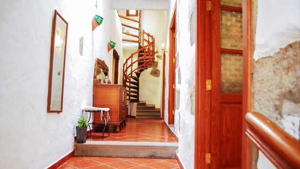Un pasillo estrecho con una escalera de madera, una pequeña mesa con una planta y una puerta con marco de madera.