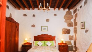 Un dormitorio con una cama de madera, dos mesitas de noche con lámparas, un armario de madera y una pared de piedra.