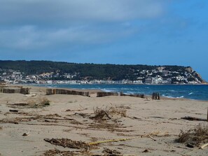 A beach with a wooden fence, sandy shore, and a town in the background. - Apartamento Reformado CON Vistas AL MAR (Torroella de Montgrí)