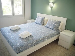 A neatly made bed with a patterned bedspread, two pillows, and folded towels on a white nightstand. - Apartamento Reformado CON Vistas AL MAR (Torroella de Montgrí)
