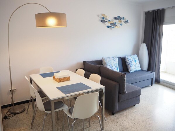 A modern living room with a dining table, chairs, a sofa, and a floor lamp. - Apartamento Reformado CON Vistas AL MAR (Torroella de Montgrí)