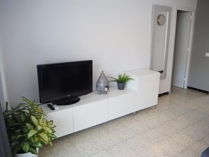 Ein modernes Wohnzimmer mit einem Flachbildfernseher auf einem weißen Schrank, einer Dekorationsvase und einer Topfpflanze.
