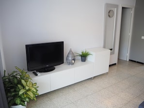 A modern living room with a flat-screen TV on a white cabinet, a decorative vase, and a potted plant. - Apartamento Reformado CON Vistas AL MAR (Torroella de Montgrí)