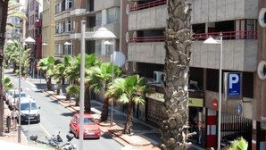 Un edificio de varios pisos con balcones, un letrero de estacionamiento y palmeras a lo largo de la calle.