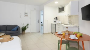 Un espacio habitable compacto con kitchenette, comedor con productos para el desayuno y sofá con planta.