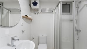 Un baño moderno con lavamanos blanco, inodoro y ducha con mampara de vidrio.