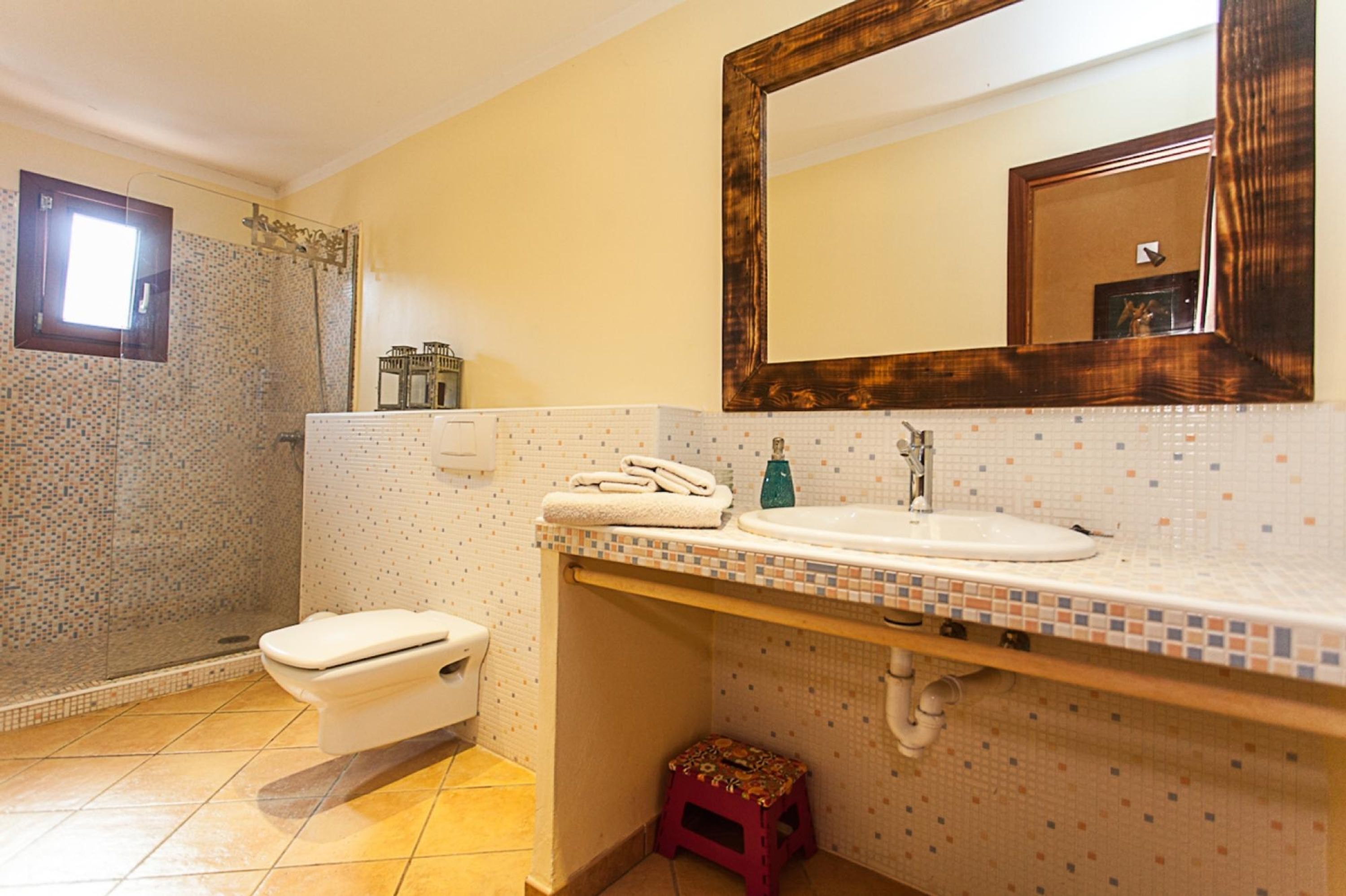 A bathroom with a toilet, sink, mirror, shower, and tiled walls.