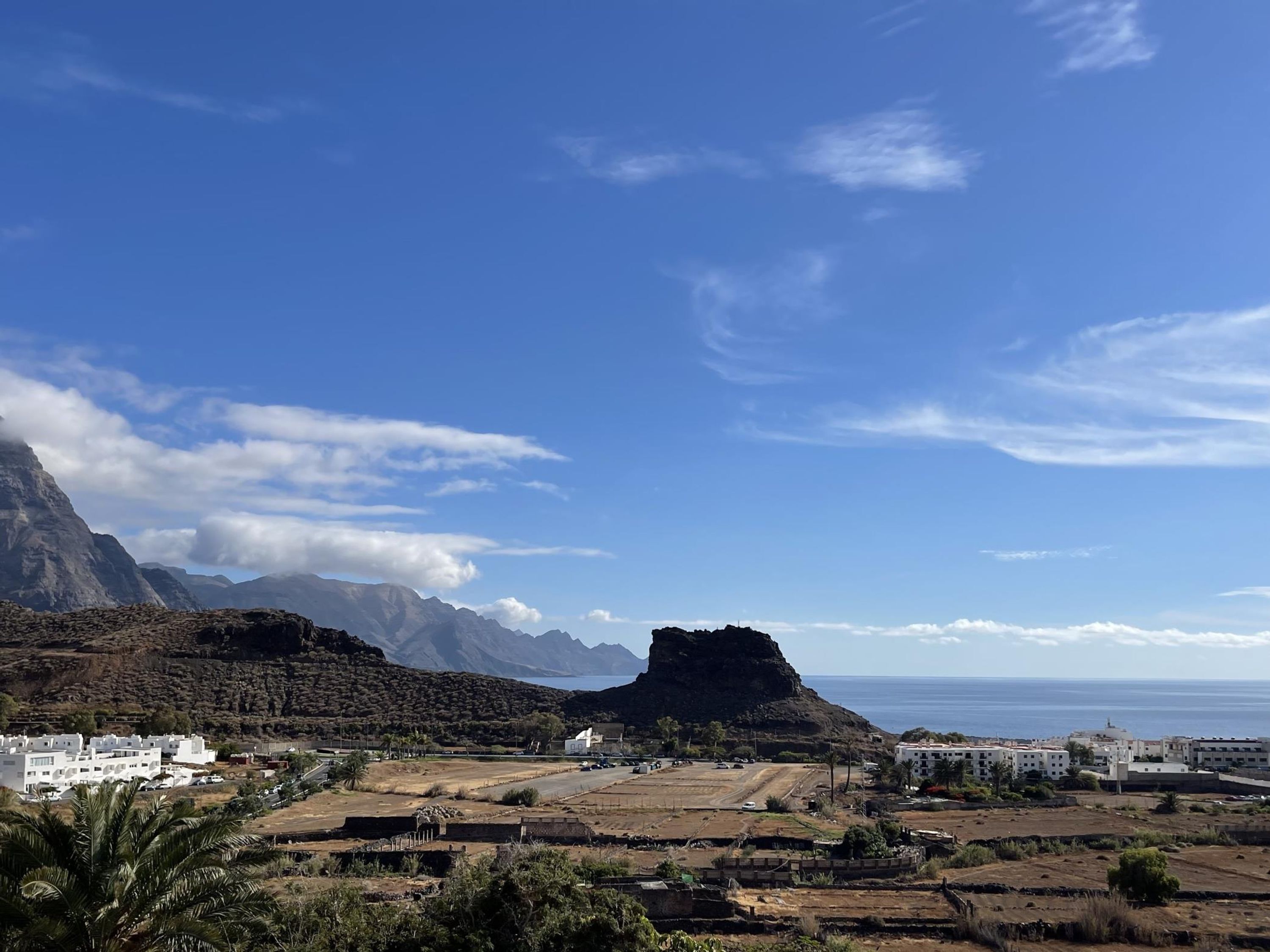 A coastal town with a prominent rocky hill, white buildings, and a clear blue sky.