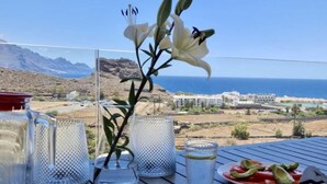 A table with a meal, a glass of water, and a flower arrangement with a view of the sea and mountains. - Apartamento Roca Paraiso DE Agaete CON Vistas (Agaete)