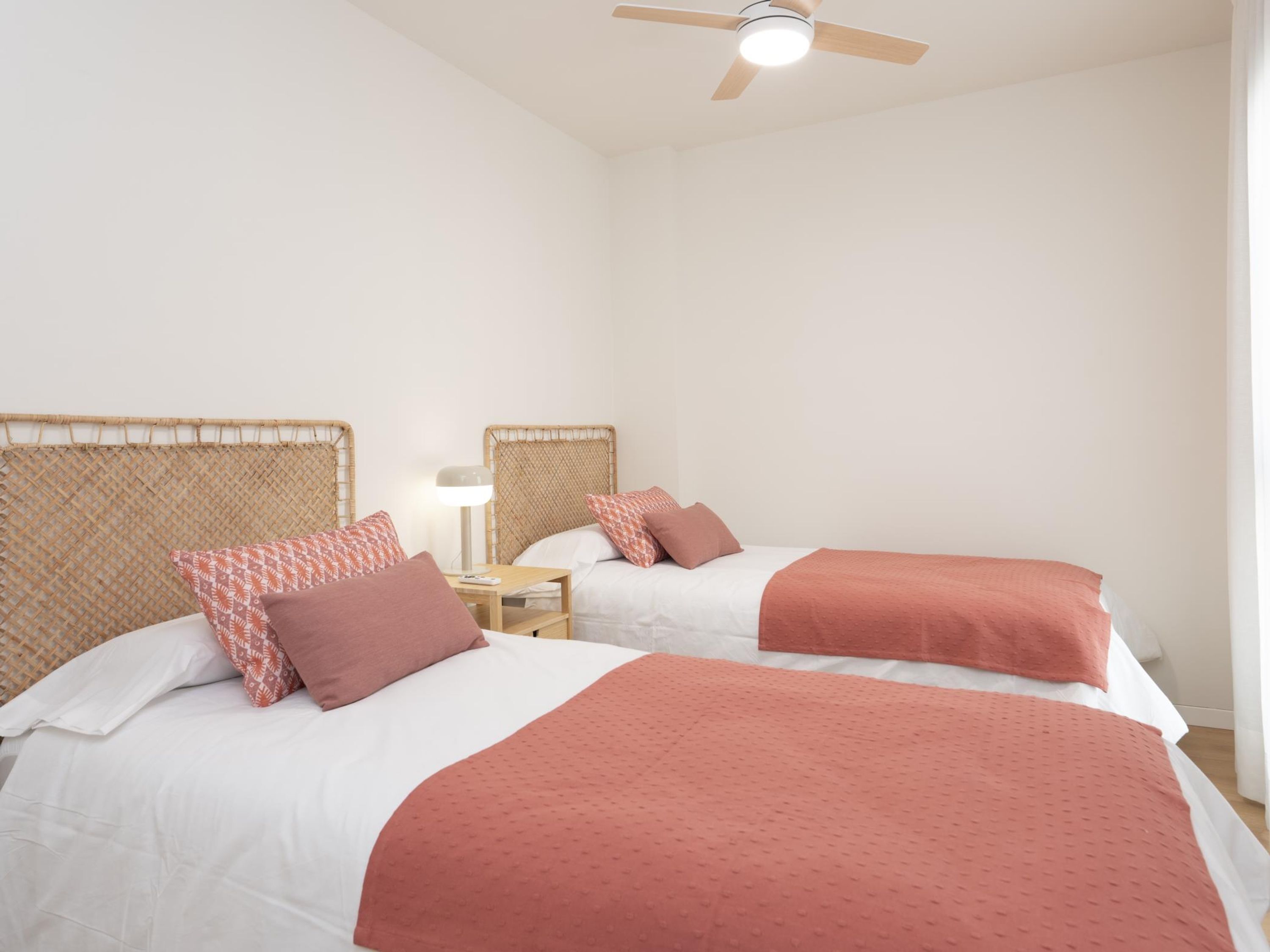 A room with two beds, each with a headboard and a bedside table with a lamp.