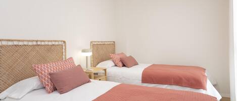 A room with two beds, each with a headboard and a bedside table with a lamp.
