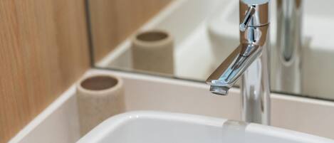Un lavamanos con grifo cromado y un espejo que refleja un rollo de papel higiénico.