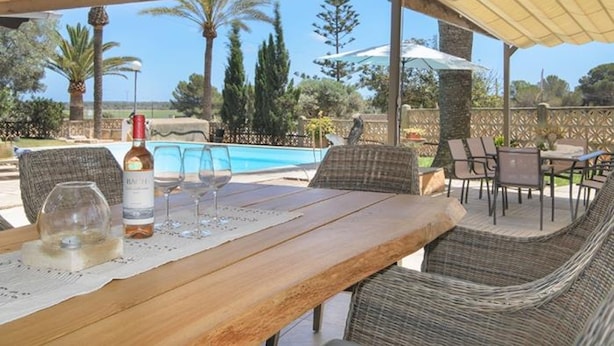 An outdoor patio with a pool, wicker furniture, and a table with wine glasses and a bottle. - CA SA Padrina in Col nia de Sant Jordi (Ses Salines)