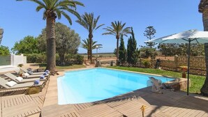 A swimming pool with wooden deck and lounge chairs, surrounded by palm trees and a clear sky. - CA SA Padrina in Col nia de Sant Jordi (Ses Salines)