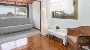 A room with a white sofa, a wicker chair, a table with a vase, and a window with a view of greenery. - CA SA Padrina in Col nia de Sant Jordi (Ses Salines)