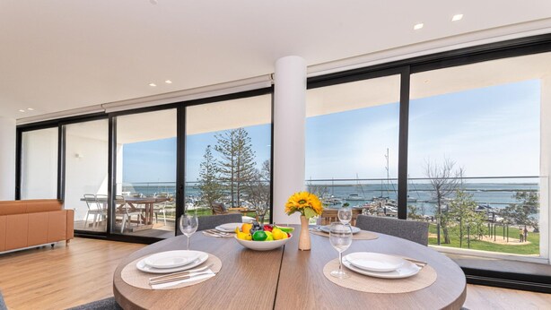 A dining area with a round table, chairs, a bowl of fruit, and a vase with flowers.