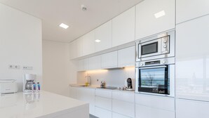 A modern kitchen with white cabinetry, a built-in oven, a microwave, and a coffee maker.