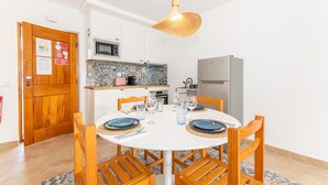A compact kitchen with white cabinets, a microwave, a refrigerator, and a dining table set for four. - Refugio da Ria 3 Mins da Praia p tio Central (Tavira)