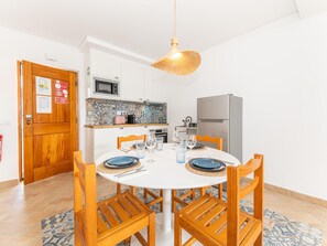 A compact kitchen with white cabinets, a microwave, a refrigerator, and a dining table set for four. - Refugio da Ria 3 Mins da Praia p tio Central (Tavira)