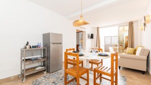 A dining area with a table set for four, surrounded by wooden chairs, a refrigerator, and a TV mounted on the wall. - Refugio da Ria 3 Mins da Praia p tio Central (Tavira)