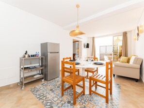 A dining area with a table set for four, surrounded by wooden chairs, a refrigerator, and a TV mounted on the wall. - Refugio da Ria 3 Mins da Praia p tio Central (Tavira)