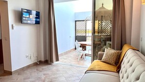 A modern living room with a flat-screen TV, a sofa, and a dining area visible through a glass door. - Refugio da Ria 3 Mins da Praia p tio Central (Tavira)