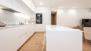 A modern kitchen with white cabinetry, a central island, and a dining area with a TV. - Waterfront Luxury On Ria Formosa (Olhao)