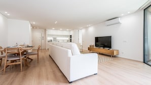 A modern living room with a sofa, dining table, chairs, a TV, and a kitchen area. - Waterfront Luxury On Ria Formosa (Olhao)