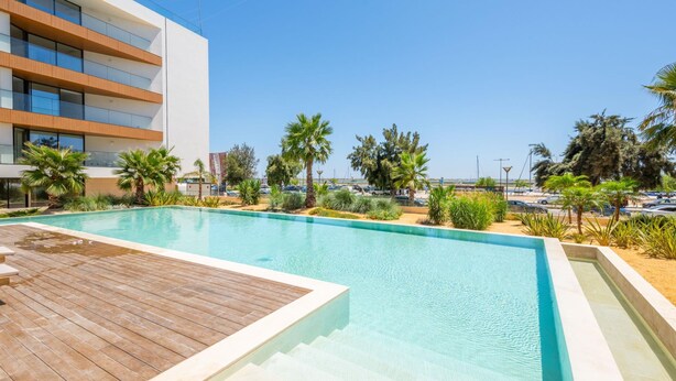 A modern hotel with a swimming pool, palm trees, and a clear blue sky. - Waterfront Luxury On Ria Formosa (Olhao)