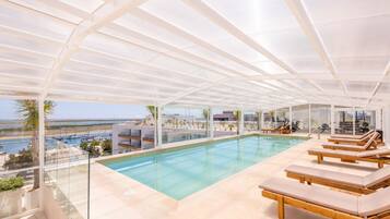 Piscina infinita no terraço com espreguiçadeiras, guarda-corpos de vidro e vista para o mar.