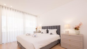 A modern bedroom with a grey bed, white linens, a bedside table with a lamp, and a nightstand with a vase. - Waterfront Luxury On Ria Formosa (Olhao)