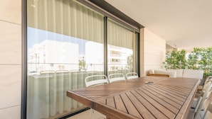 A modern outdoor dining area with a wooden table and chairs, large windows, and a view of buildings. - Waterfront Luxury On Ria Formosa (Olhao)
